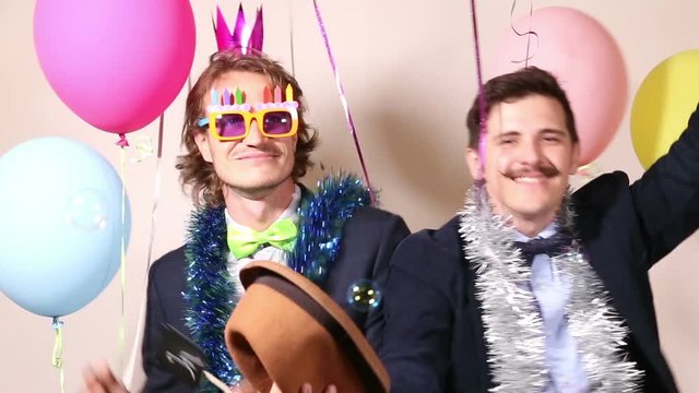 Two cheerful men holding sign in love and dancing in photo booth