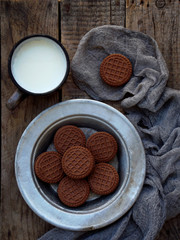 chocolate cookies with white cream and cup of milk on wooden background. Selective focus.