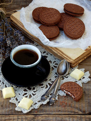 Romantic composition of chocolate cookies with white cream, cup of coffee and bouquet lavender on wooden background. Selective focus.