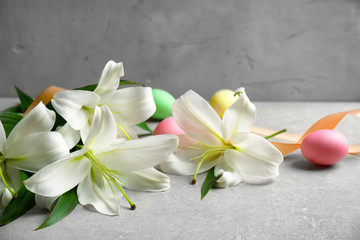 Obraz na płótnie Canvas Beautiful lilies, eggs and ribbon on gray table