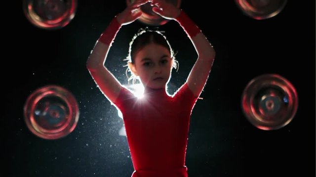 Little child girl dance on the stage in red dress on a background scenes turns bright light - slow motion