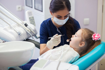 female dentist in mask treats teeth little girl