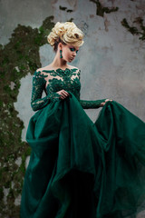 Portrait of young attractive blonde woman in a beautiful green dress. Textured background, interior. Luxury hairstyle