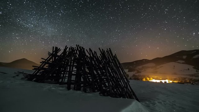Night sky with stars moving over winter rural country with wooden frame, astronomy time lapse, dolly shot over snow