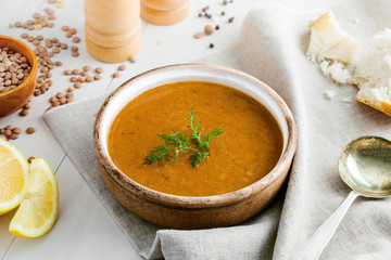 Bowl of delicious lentil soup with bread and lemon slice on a white wooden table. Traditional healthy vegetarian food. Top view.