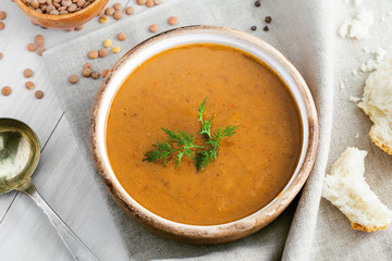 Soup made of lentil and vegetables in a rustic bowl on a canvas tablecloth. Delicious healthy vegetarian food on a white wooden table. Top view.