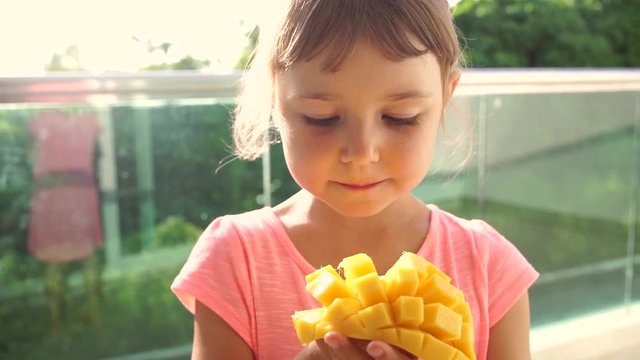 Close-up of 5 year old girl girl eating ripe cut into strips mango.