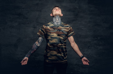 A man with tattoos on his neck, face and arms, dressed in a camouflage t shirt.