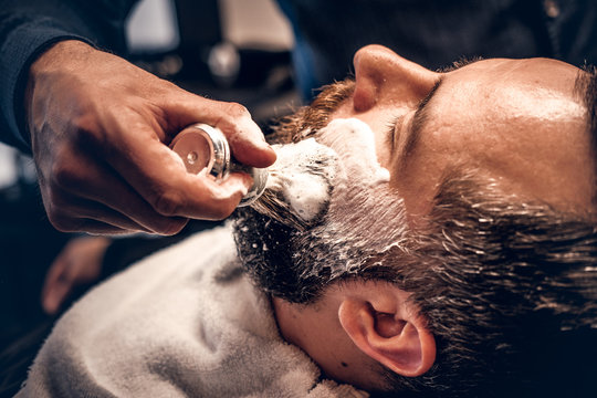 Barber applies shaving foam to a man's face in a saloon.