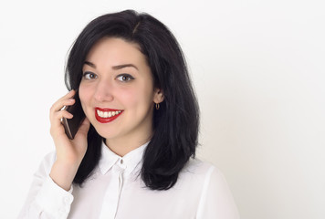 Beautiful business woman in a white blouse and with bright red lipstick on her lips talking on her mobile phone. She smiles a snow-white smile and enjoys a successful conversation.