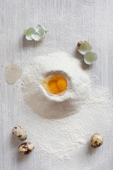 Fototapeta na wymiar Sifted flour and quail eggs on the light wooden table