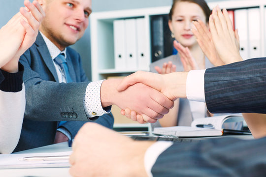 Business handshake. Close-up of two young man shaking hands with smile while sitting at office with their beautiful coworker.