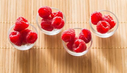 raspberries in small bowls on a wooden background.
