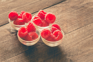 raspberries in small bowls on a wooden background.