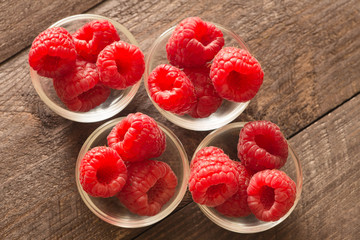 raspberries in small bowls on a wooden background.