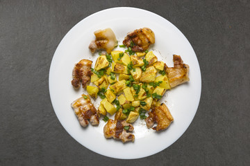 Fried potatoes with meat in a white plate on Black table