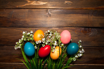 Obraz na płótnie Canvas Multi-colored, bright Easter eggs with green, spring lilies of the valley on wooden background
