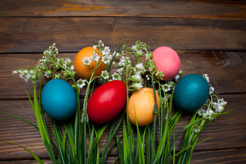 Multi-colored, bright Easter eggs with green, spring lilies of the valley on wooden background