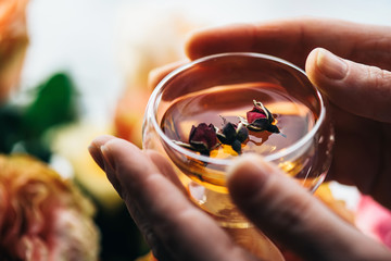 Human hands holding glass of Fresh herbal tea with dry rose buds