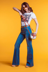 Beautiful young brunette girl wearing white t-shirt jeans flared with a small bag standing on a yellow background in the Studio..Bright stylish look