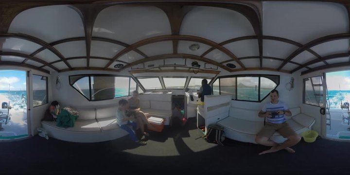 360 VR video. Inside view of sailing yacht with family and captain. Father taking mobile photos of son and wife. Sea travel during vacation on Mauritius Island