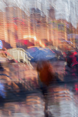 Abstract background of Lonely Girl under umbrella in the, street in rain. Light illumination from lanterns, shop windows. Impressionism style. Intentional motion blur