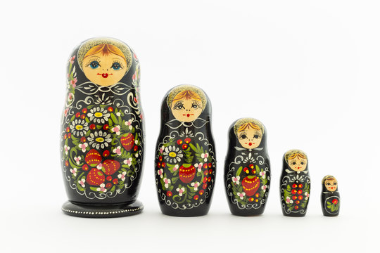Beautiful black matryoshka dolls with white, green and red painting in front of light background