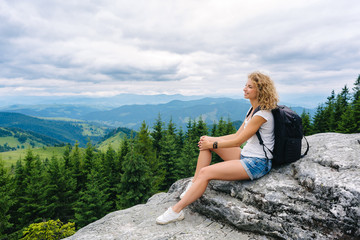 A young woman stands on top of a mountain in cloudy weather enjoying the view