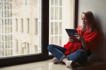 Portrait of a young girl reading an e-book at the window
