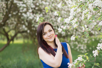 Naklejka na ściany i meble beautiful young brunette woman standing near the blossoming apple tree on a warm spring day