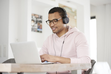 Enjoy music. Shot of a handsome young Afro American man using his laptop and listening music while working at home.
