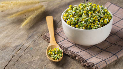 dried  chamomile in a white bowl with wooden spoon on wooden table view from above