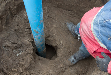 A worker stands near the blue pipe that sticks out from the Earth