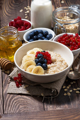 homemade oatmeal with berries and wooden background, vertical