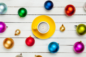 Naklejka na ściany i meble photo of yellow cup of coffee near colorful beautiful baubles on the wonderful white wooden background