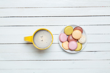 photo of yellow cup of coffee and plate full of macaroons on the wonderful white wooden background