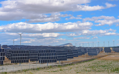 Naklejka premium Field of solar panels and wind turbines with cloudy sky