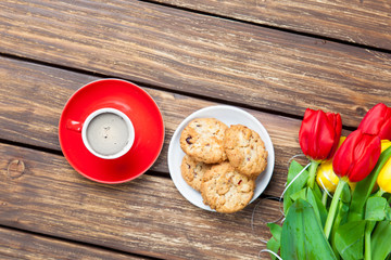 bunch of tulips, plate full of cookies and cup of coffee on the wonderful brown wooden background