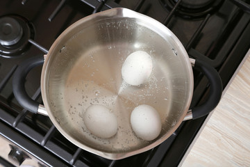 White eggs in boiling water into saucepan on the gas stove
