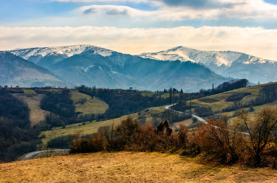 high mountain ridge with snowy peaks. hillside with forest in springtime. road winds through rural fields. Beautiful Carpathian nature. High altitude spectacular view.