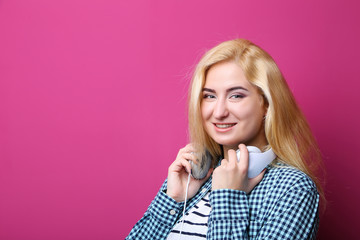 Young woman listening music with headphones on pink background