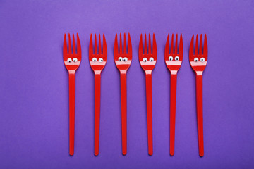 Red plastic forks with googly eyes on a purple background