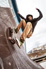  A teenage skater in a sweatshirt and jeans rides the wall on a skateboard in a skatepark, © yanik88