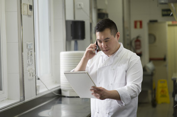 Fototapeta premium Chinese cook speaks with smartphone and notebook