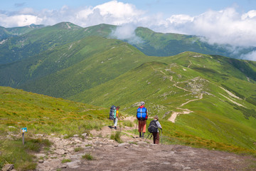 Fototapeta na wymiar Travelers with backpacks are walking down the ridge