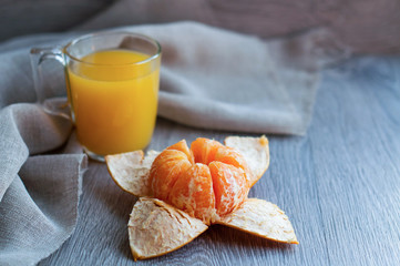 Fototapeta na wymiar Mandarin and fresh vitamin juice in a glass cup, on a gray, wooden background.