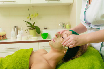 Beautician wiping off green mask on woman