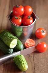 Tomatoes in a small bucket and cucumbers on a wooden background