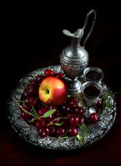 Still life with fresh cherries and a peach placed in silver plate on dark background.
