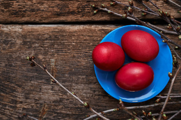 Three Easter eggs, on a blue plate in the nest with spring branches